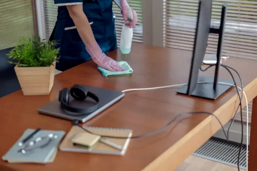 Empleado agencia de limpieza limpiando escritorio de trabajo